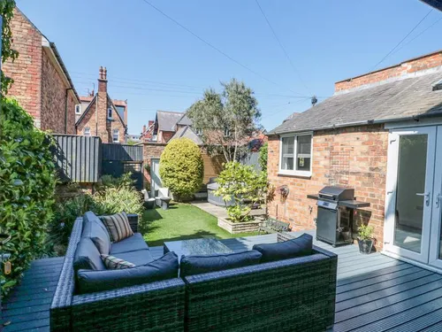 Enclosed garden with decking, rattan outdoor sofa, lawn, and bi-fold doors from the dining room