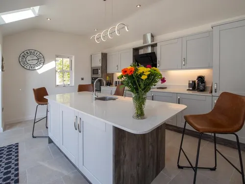 Kitchen with grey shaker units, quartz-topped island, leather bar stools, and skylight