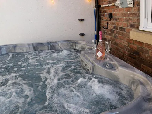 Hot tub bubbling on the enclosed patio with prosecco and glasses on the edge at Salt Bay