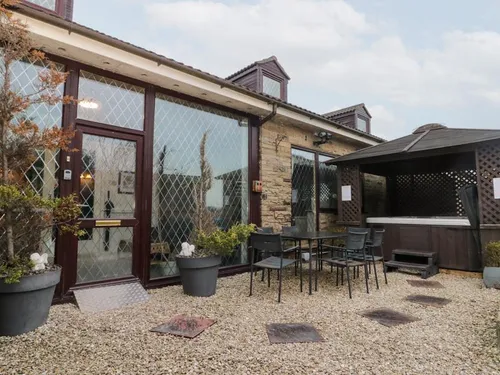 Rear patio with metal garden furniture and covered hot tub beside stone-fronted conservatory windows