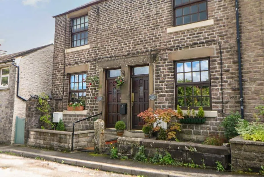 Shenton Cottage stone exterior with hanging baskets and potted plants by the entrance