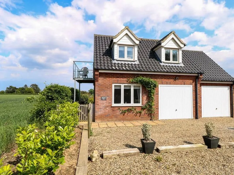 Spinney's Den red-brick cottage with balcony overlooking fields and gravel driveway