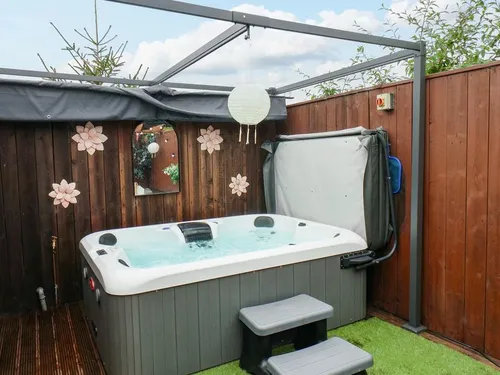 Hot tub in enclosed garden with timber fencing, pergola frame, and wooden decking