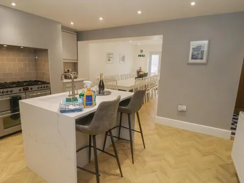 Kitchen with marble-effect island, bar stools, range cooker, and herringbone floor leading to a long dining table