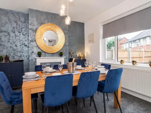 Dining room with oak table set for six, blue velvet chairs, grey marbled feature wall, and gold circular mirror