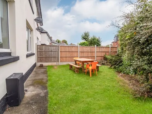 Enclosed back garden with wooden picnic table on the lawn and timber fence panels