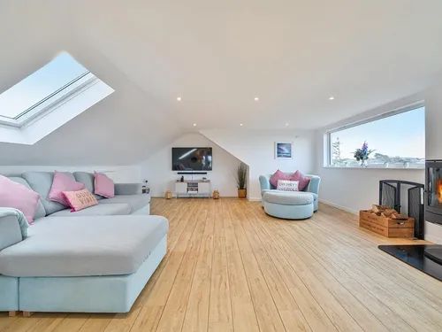 Cottage lounge with skylight, wood burner, corner sofa and TV on wall
