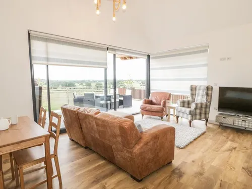 Open-plan living area with leather sofa, tartan wingback chair, bi-fold doors, and Somerset Levels views