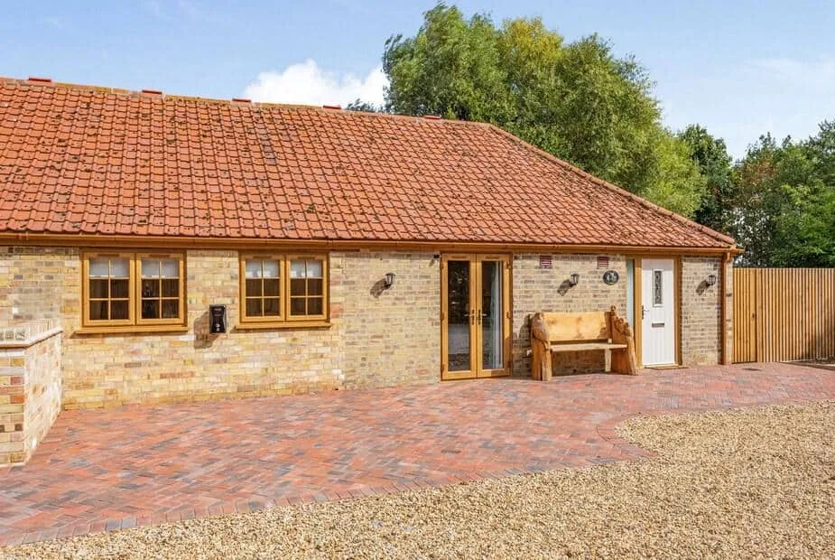 Tawny Acre Barn brick cottage exterior with tiled roof and wooden bench by entrance.