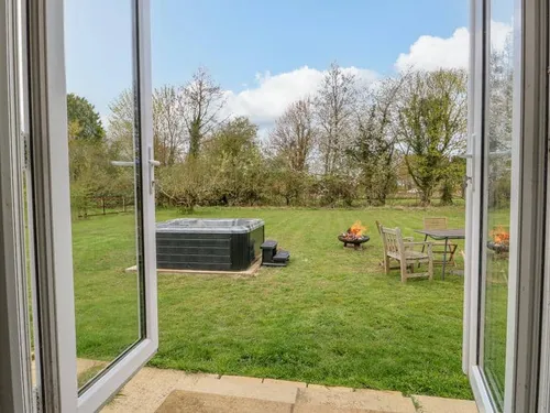 Cottage garden with hot tub, fire pit and outdoor seating seen through open doors