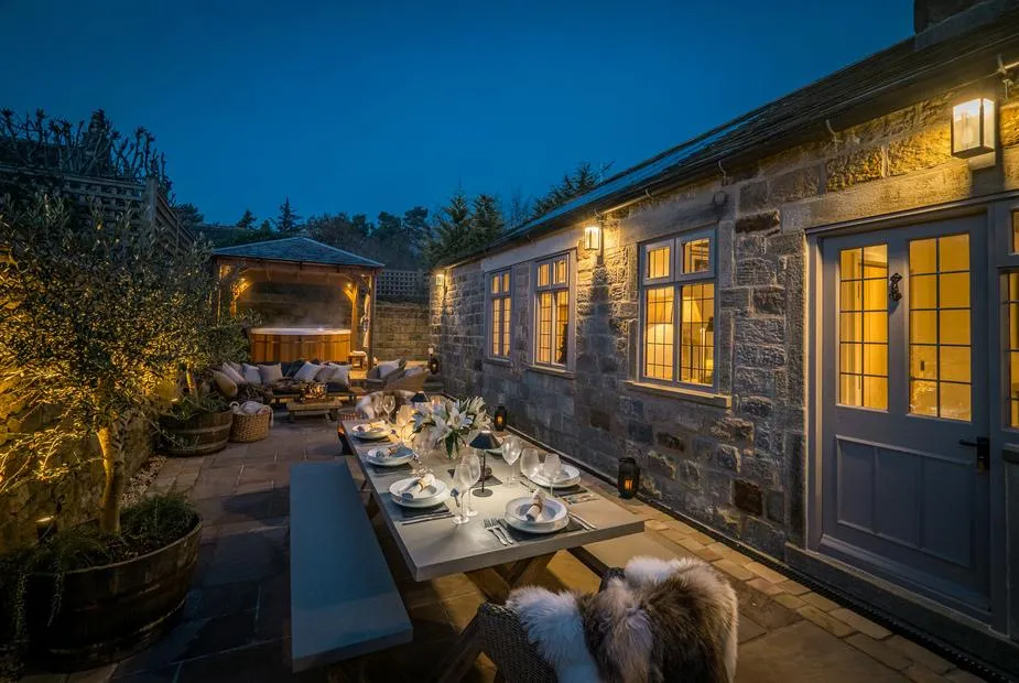 The Brew House stone exterior with outdoor dining area and covered hot tub at dusk.