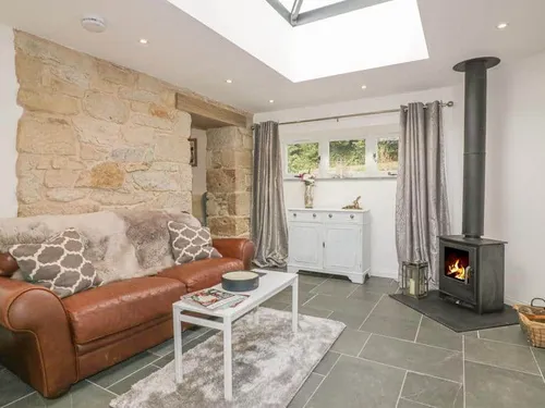 Cottage lounge with leather sofa, stone wall and wood-burning stove