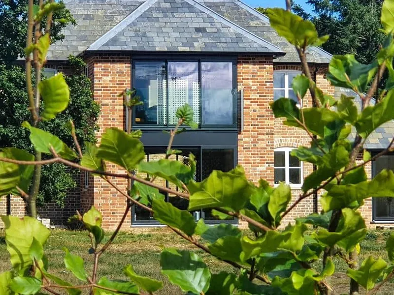 Red brick The Coach House with large windows, seen through leafy branches in the foreground.