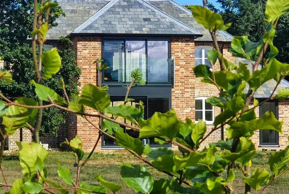 Red brick The Coach House with large windows, seen through leafy branches in the foreground.