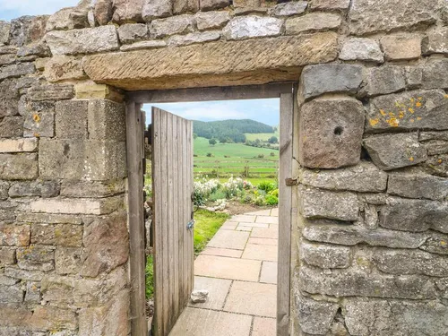 Cottage stone wall with wooden gate opening to garden and countryside view