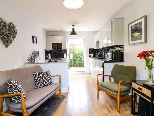 Cottage living area with sofa, armchair and modern kitchen leading to patio garden