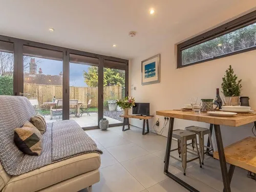 Cottage living area with sofa, dining table and doors opening to garden patio with seating