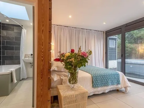 Cottage bedroom with vase of flowers, ensuite bathroom, and glass doors to patio