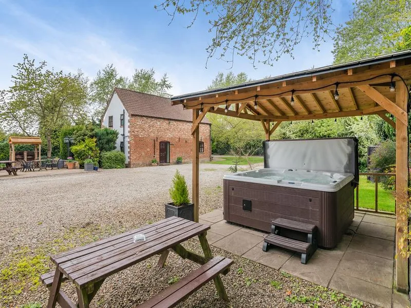 Courtyard with hot tub under wooden pergola and converted farm buildings at Hopgrove Farm