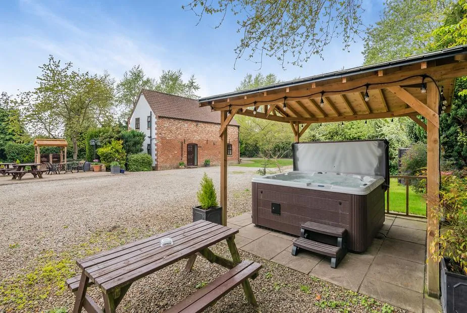 Courtyard with hot tub under wooden pergola and converted farm buildings at Hopgrove Farm