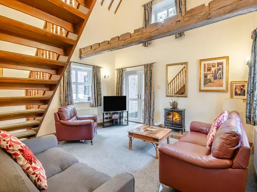 Living room with open wooden staircase, exposed beam, leather sofas and electric fire