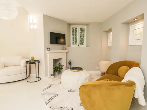 Cottage lounge with mustard armchair, round ottoman and wall-mounted TV above fireplace