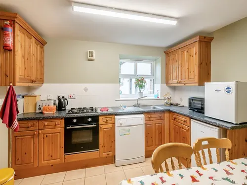 Kitchen with pine cabinets, gas hob, oven and dishwasher alongside a dining table