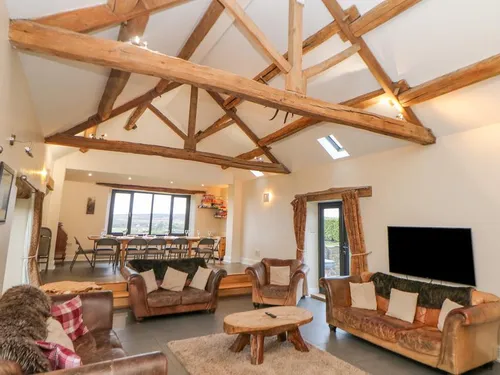 Open-plan living room with exposed oak roof beams, leather sofas, and dining area beyond