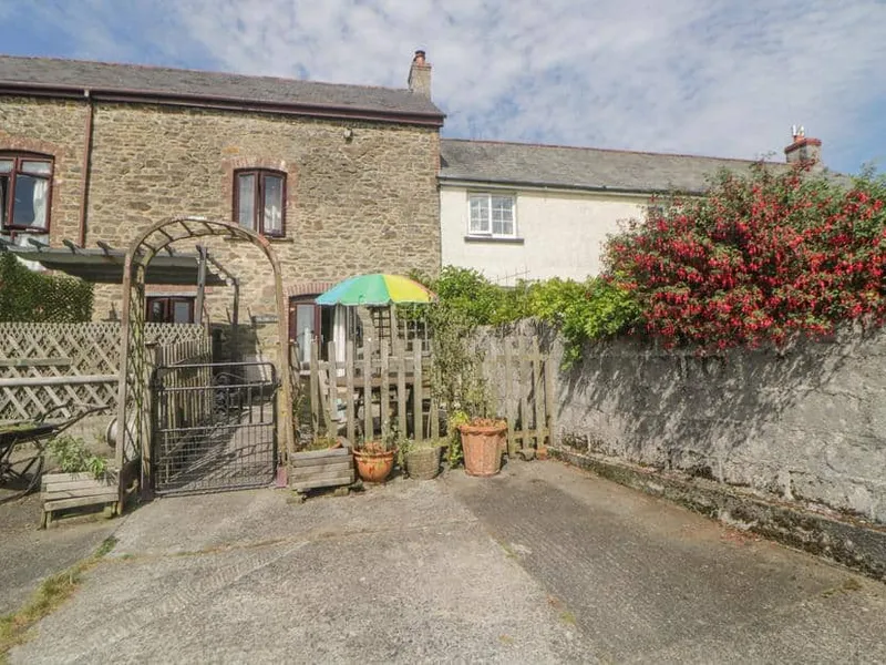 Stone-walled The Orchard cottage with patio, wooden gate and colourful umbrella.