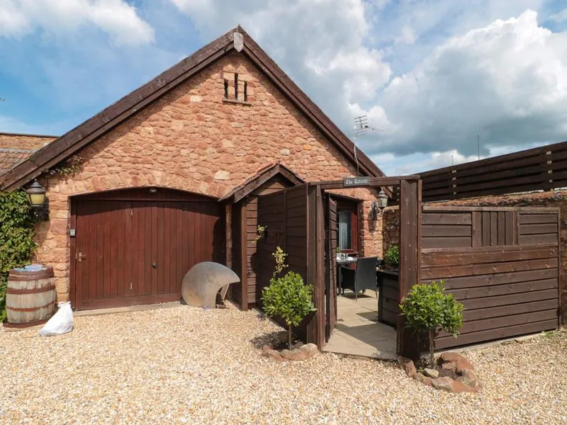 The Retreat red sandstone cottage with arched wooden garage door and gravel courtyard in Washford