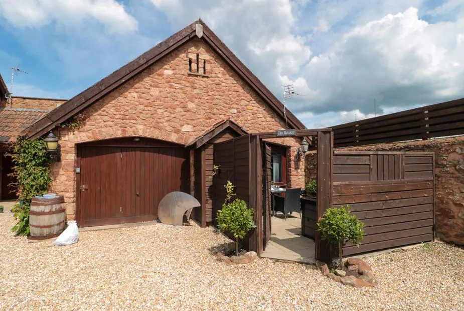 The Retreat red sandstone cottage with arched wooden garage door and gravel courtyard in Washford