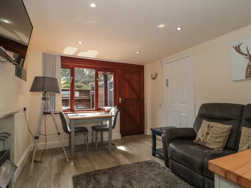 Open-plan living room with dark leather sofa, dining table for two, wall-mounted TV, and stable door to courtyard