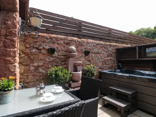 Enclosed courtyard with hot tub, rattan dining set, stone water feature, and red sandstone walls