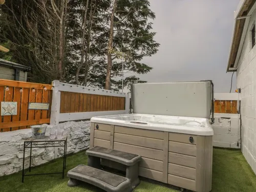 Hot tub in an enclosed corner with artificial grass, wooden fence, and trees behind