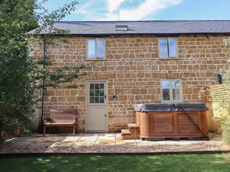 Stone exterior of The Stables with hot tub and garden bench on patio