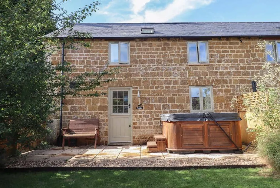 Stone exterior of The Stables with hot tub and garden bench on patio