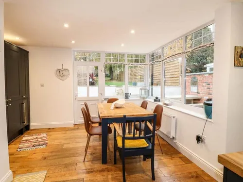 Cottage dining area with wooden table and chairs by large windows and patio door