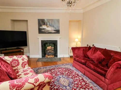 Cottage lounge with red sofas, fireplace and patterned rug