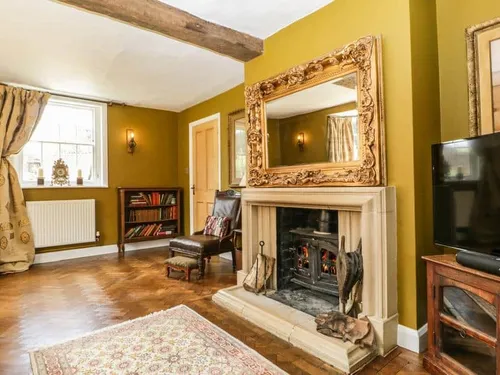 Cottage lounge with wood-burning stove, ornate mirror and exposed ceiling beam