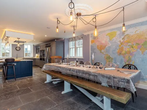 Rustic dining table with bench seating, world map wall, and shaker kitchen with blue island