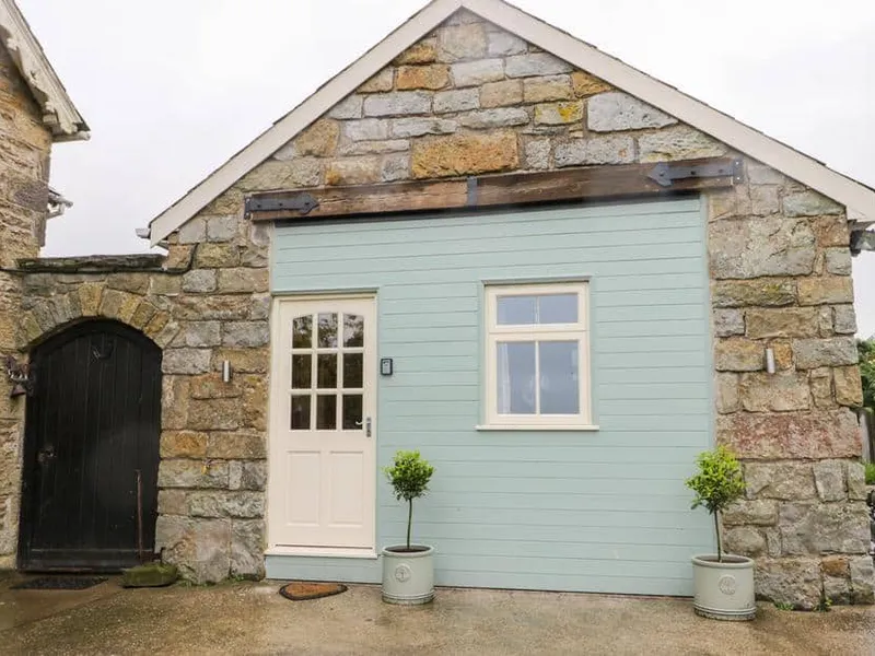 Stone exterior of Wagtail Nest, Northfield Cottage with pastel door and two potted trees