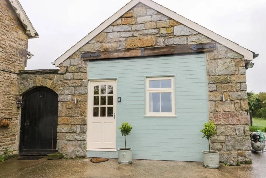 Stone exterior of Wagtail Nest, Northfield Cottage with pastel door and two potted trees