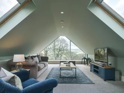 Cottage loft living room with sofas, TV unit and large triangular window