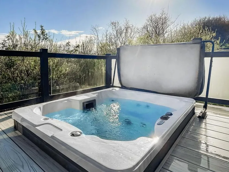 Hot tub on wooden decking with glass panels and Mendip hillside greenery behind