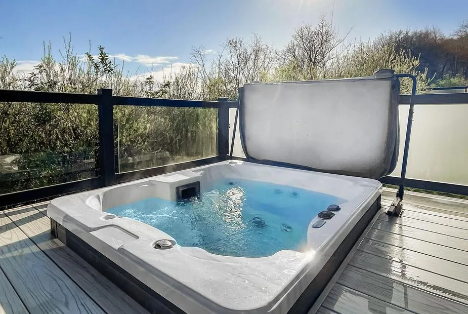 Hot tub on wooden decking with glass panels and Mendip hillside greenery behind