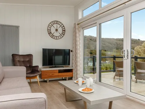 Lodge living room with sofa, armchair, TV, and patio doors to countryside views