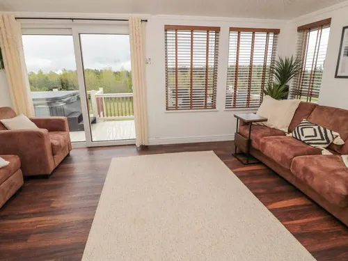 Lodge living room with brown sofas and sliding door to deck with hot tub