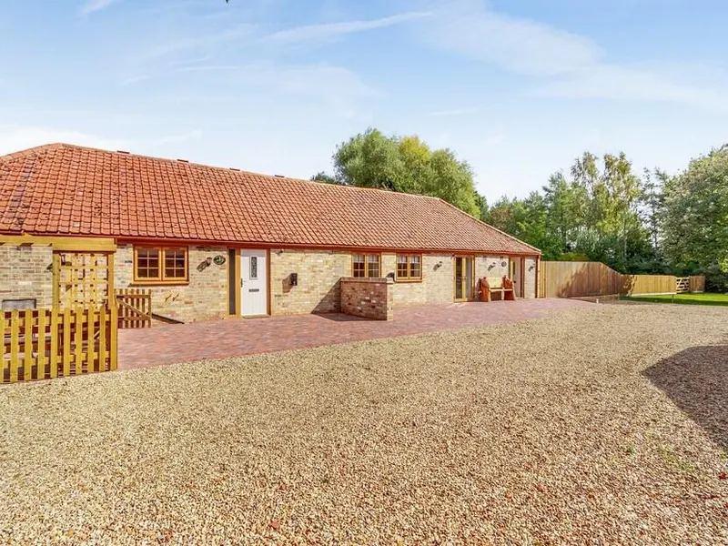 Woodpecker Barn with red tiled roof, brick patio and gravel driveway, trees in background