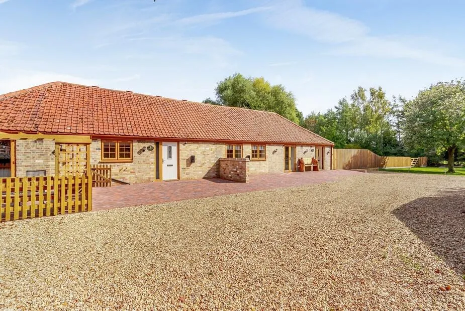 Woodpecker Barn with red tiled roof, brick patio and gravel driveway, trees in background