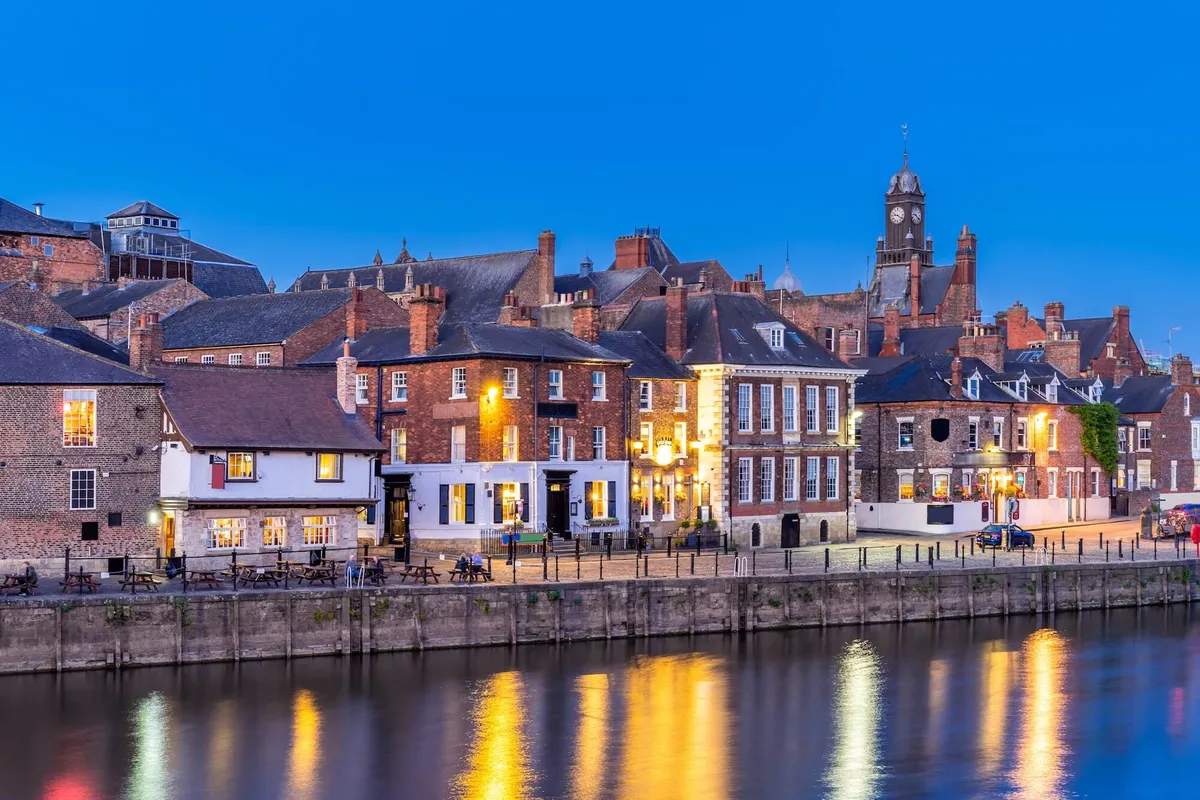 Warm lights from riverside pubs reflecting in the River Ouse in York at dusk